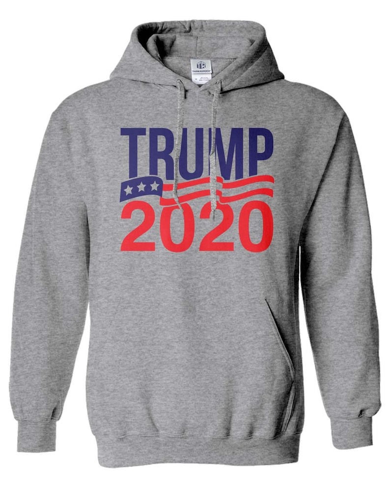 May include: Grey hooded sweatshirt with the text "TRUMP 2020" in red and blue lettering. The text is overlaid with a stylised American flag design.