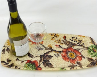 May include: A floral patterned serving tray with a wine bottle and a wine glass on top. The tray is made of a hard, plastic-like material and has a light brown background with red, green, and yellow flowers.