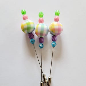 May include: Three pastel plaid fabric covered pins with green, pink, and yellow accents. Each pin has a blue crystal bead and a silver pin.
