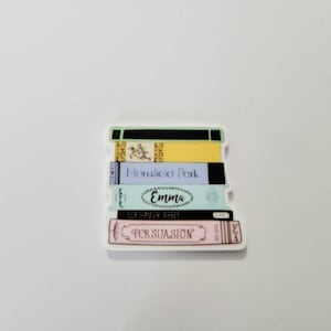 May include: A stack of five books with colorful covers. The titles of the books are "Persuasion", "Northanger Abbey", "Emma", "Mansfield Park", and a title that is not visible.