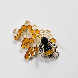 May include: A gold-toned bee brooch with black and yellow enamel details, perched on a honeycomb design.