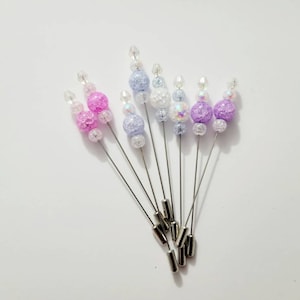 May include: A set of six beaded pins with silver metal bases. The beads are in shades of pink, purple, and white.