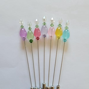 May include: Set of seven pastel colored glass teardrop shaped pins with clear crystal accents. The pins have silver metal stems.