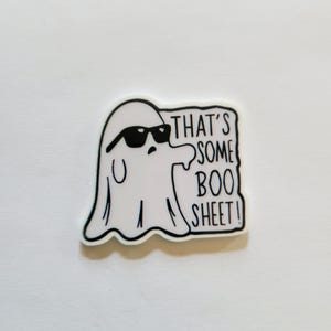 May include: A white ghost wearing sunglasses with the phrase "THAT'S SOME BOO SHEET!" in black text. The ghost has a black outline and is on a white background. The sticker is a fun, spooky Halloween-themed item.