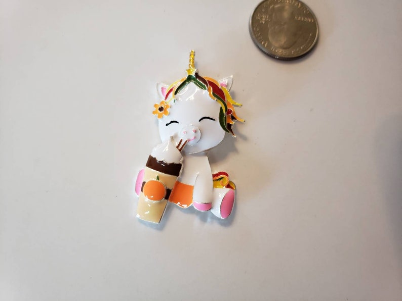 May include: A white unicorn figurine with a colorful mane, flower crown, and a pumpkin spice latte. The unicorn is holding the latte and has a happy expression. The figurine is approximately 1.5 inches tall.