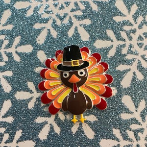 May include: A cartoon turkey wearing a black pilgrim hat with a brown buckle. The turkey has a red, orange, and yellow fan-shaped tail.