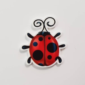 May include: A red and black ladybug with black dots and blue accents. The ladybug has a white background and a white outline.