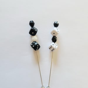 May include: Two lapel pins with dice-themed designs. One pin features a black and white color scheme, while the other has a white and black color scheme. Each pin has a silver-colored metal base and a series of beads.
