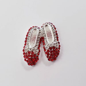 May include: A pair of red and silver jeweled slipper charms. The slippers are decorated with red rhinestones and have a silver bow.