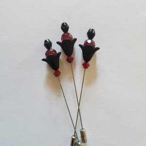 May include: Three decorative pins with black tulip-shaped heads, red bead accents, and silver-colored pins. Each pin features a black bead and a red crystal bead. The pins are arranged on a white surface.