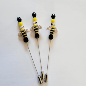 May include: Three silver bee brooches with black and yellow bead accents. Each brooch features a ceramic bee with black and yellow stripes.