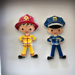 May include: Two colorful, cartoon-style figurines of a firefighter and a police officer. The firefighter wears a red helmet and yellow uniform. The police officer is in a blue uniform and hat. Both have their hands on their hips.