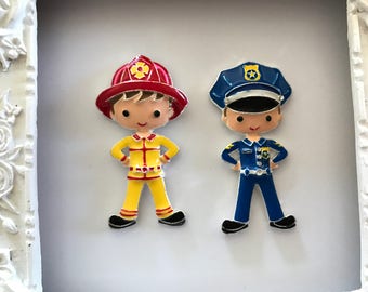 May include: Two colorful, cartoon-style figurines of a firefighter and a police officer. The firefighter wears a red helmet and yellow uniform. The police officer is in a blue uniform and hat. Both have their hands on their hips.
