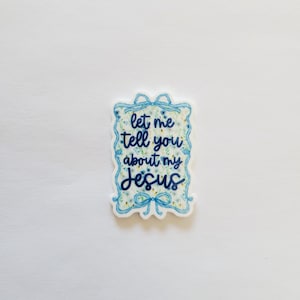 May include: A white sticker with a blue floral border and the text "let me tell you about my Jesus" in a handwritten style. The sticker has a light blue background with a floral pattern.