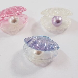 May include: Three open clam shell ornaments with pearls inside. The shells are translucent and come in pink, white, and purple.