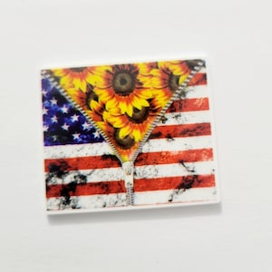 May include: Square-shaped decorative item featuring an American flag design with a zipper revealing sunflowers. The flag has red and white stripes and a blue field with white stars. The sunflowers are yellow and brown.