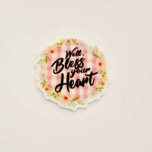 May include: A round, white, pink and green floral resin cabochon with the text "Well, Bless your Heart" in black.
