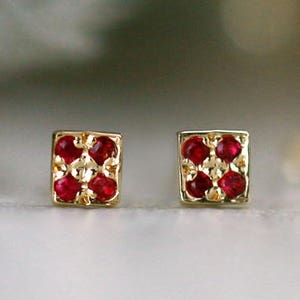 May include: A pair of gold earrings with a square design featuring red ruby stones.