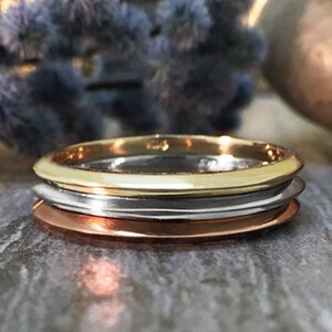 May include: Three stacked rings, one gold, one silver, and one copper. The rings are all smooth and shiny.