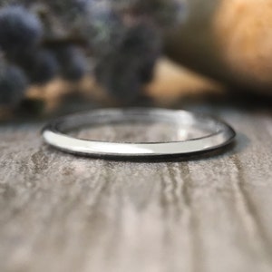 May include: A thin silver band ring, shown on a wooden surface.