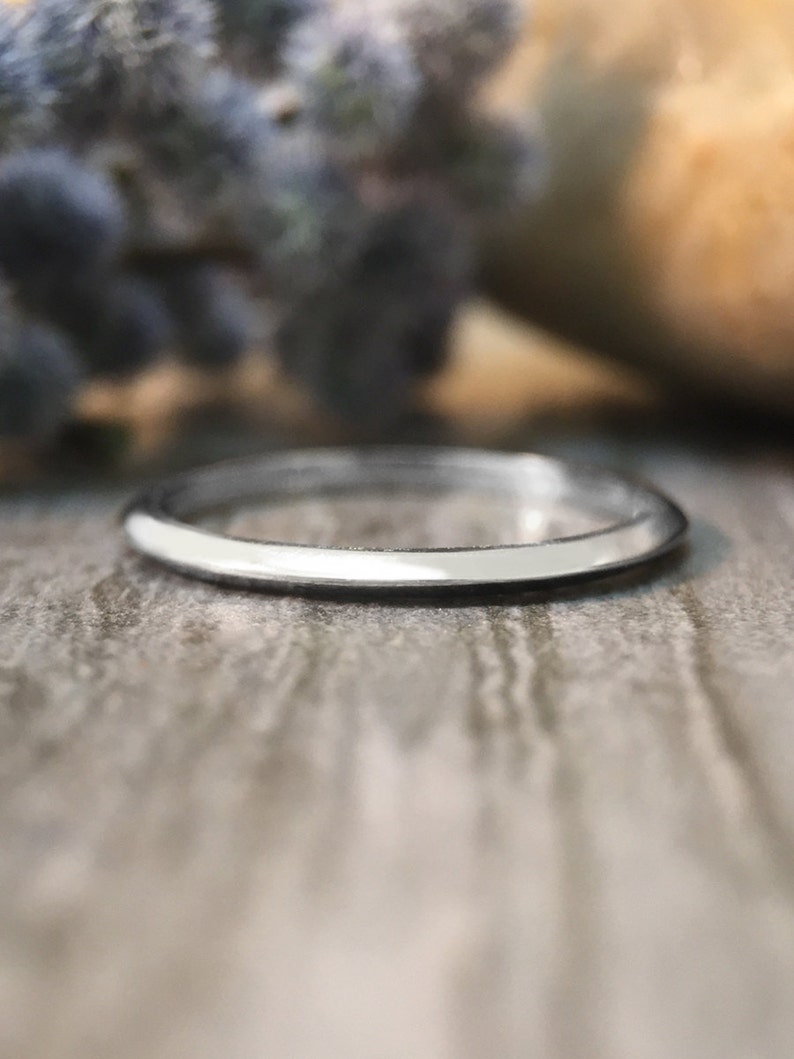 May include: A thin silver band ring, shown on a wooden surface.