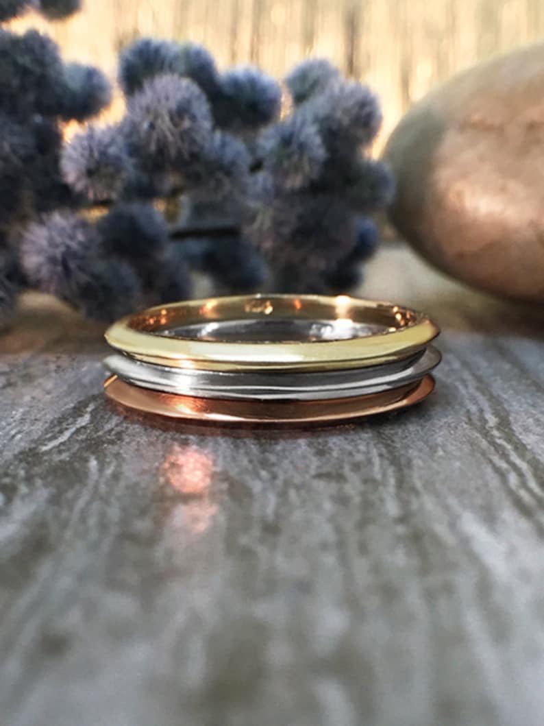 May include: Three stacked rings, one gold, one silver, and one copper. The rings are all smooth and shiny.
