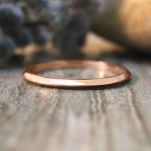 May include: A simple, polished, rose gold band ring.