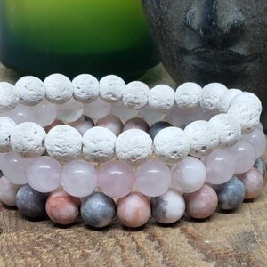 May include: Three stacked bracelets featuring white lava rock beads, pink rose quartz beads, and pink and grey agate beads.