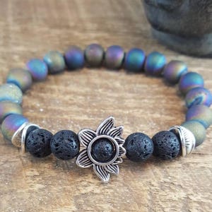 May include: A bracelet made of iridescent blue and black beads with a silver sunflower charm. The bracelet is on a wooden surface.