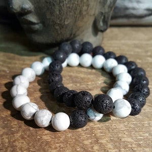 May include: Two bracelets made of black lava rock beads and white howlite beads. The bracelets are stacked on top of each other.