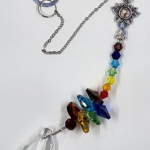 May include: A crystal suncatcher with a rainbow of crystals hanging from a silver chain. The chain is attached to a silver swirl design.
