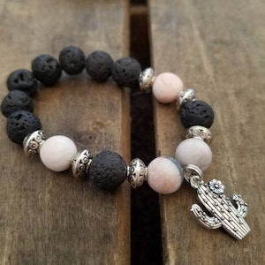 May include: A black lava rock and pink stone beaded bracelet with a silver cactus charm.