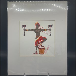 May include: A digital illustration of a person with brown skin, wearing a red and yellow skirt, a crown, and holding two axes. The person is standing on a drum with the signature "Rulo Meda" written below. The image is framed in a white mat and black frame.