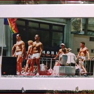 May include: A framed photograph of a group of people standing on a platform. The people are wearing swimsuits and are smiling. The photograph is taken in front of a building with a sign that says "Upper East Side".