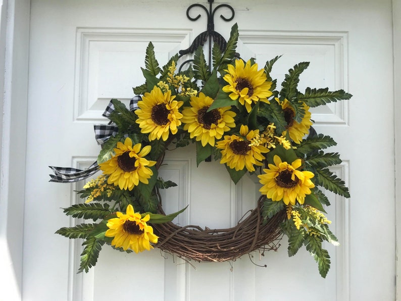 Pu&ograve; includere: Una ghirlanda di girasoli con nastro a quadri bianco e nero. La ghirlanda &egrave; realizzata in vite e presenta girasoli e verde artificiali.