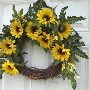Pu&ograve; includere: Una ghirlanda di girasoli con una base di vite marrone. La ghirlanda &egrave; decorata con girasoli gialli e felci verdi.