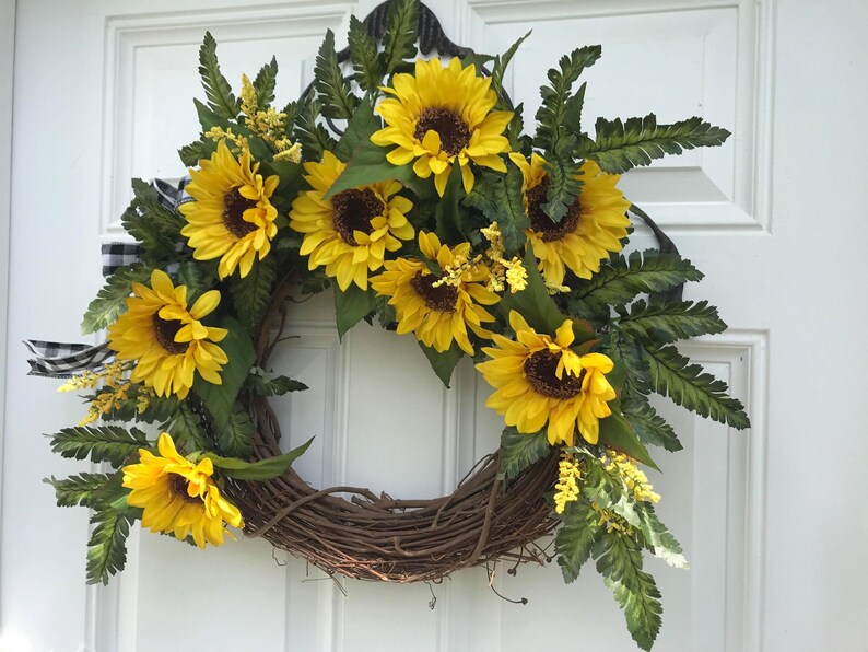 Pu&ograve; includere: Una ghirlanda di girasoli con una base di vite marrone. La ghirlanda &egrave; decorata con girasoli gialli e felci verdi.