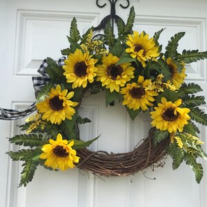 Pu&ograve; includere: Una ghirlanda di girasoli con un nastro a quadri bianco e nero. La ghirlanda &egrave; realizzata in vite e presenta una variet&agrave; di girasoli di diverse dimensioni e stadi di fioritura.