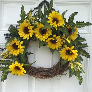Pu&ograve; includere: Una ghirlanda di girasoli con un nastro a scacchi bianco e nero. La ghirlanda &egrave; realizzata in vite e presenta diversi girasoli con petali gialli e centri marroni. La ghirlanda &egrave; decorata con foglie di felce verdi.