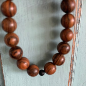 May include: A brown wooden beaded necklace with a black bead accent. The beads are round and have a natural wood grain pattern.
