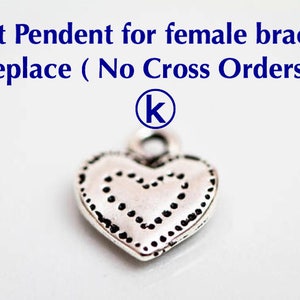 May include: Silver heart charm with a dotted design. The charm has a loop at the top for attaching to a bracelet or necklace. The charm is labeled with the letter "K".