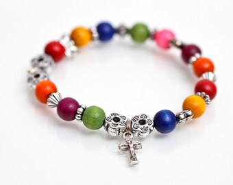 May include: A colorful wooden bead bracelet with a silver cross charm. The beads are in a rainbow pattern, with red, orange, yellow, green, blue, and purple beads.