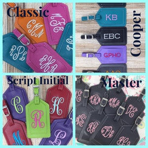 May include: A collection of rectangular luggage tags in various colors including orange, pink, teal, purple, red, lime green, and dark gray. Each tag features embroidered monograms or initials in contrasting thread and includes a silver metal buckle.