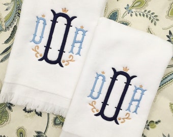 May include: Two white hand towels with fringed edges, each embroidered with a monogram in a navy blue, light blue, and gold thread. The monogram is a stylized letter "D" with a crown on top.