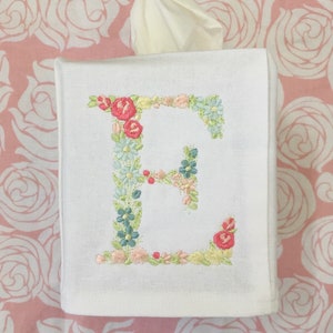 May include: White tissue box cover with a floral embroidered letter E. The embroidery is in shades of pink, green, and blue.