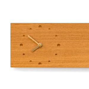 Peut inclure: Une horloge murale en bois avec un design simple. Le cadran de l'horloge est en bois avec de petits trous pour les repères des heures. Les aiguilles sont dorées.