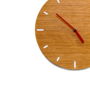 Könnte beinhalten: Eine Holzuhr mit einem roten Stundenzeiger und weißen Minutenmarkierungen. Das Zifferblatt der Uhr ist aus hellbraunem Holz mit einer Holzmaserung.