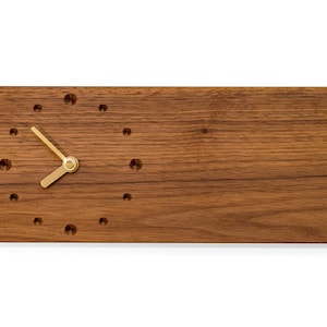 Könnte beinhalten: Eine Wanduhr aus Holz mit einem goldfarbenen Stunden- und Minutenzeiger. Das Zifferblatt der Uhr ist aus Holz mit kleinen Löchern für die Zahlen.