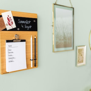 Könnte beinhalten: Ein Holz-Notizbrett mit einem Kreidetafel-Bereich, einer Klemmbrett mit einer Checkliste und zwei Bleistiften. Der Kreidetafel-Bereich hat den Text "Sommerfest 4. August" darauf geschrieben. Die Checkliste enthält die folgenden Punkte: "Mark", "Salat", "Tomaten", "Gurken", "Kartoffeln", "Kräuter".