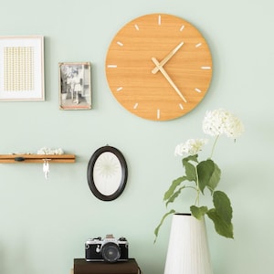 Pode incluir: Uma parede verde claro com um relógio de madeira, um suporte para chaves, uma foto emoldurada e um vaso com flores brancas. O relógio tem um mostrador de madeira clara com marcas brancas e um ponteiro de hora e minuto dourado.